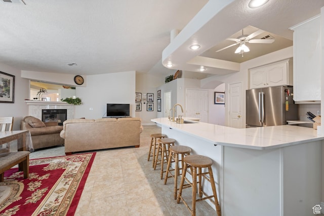 kitchen with freestanding refrigerator, arched walkways, a sink, a kitchen bar, and white cabinets