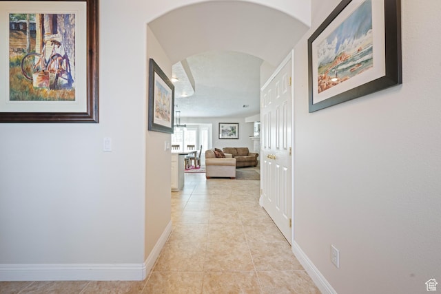 hall with arched walkways, baseboards, and light tile patterned floors