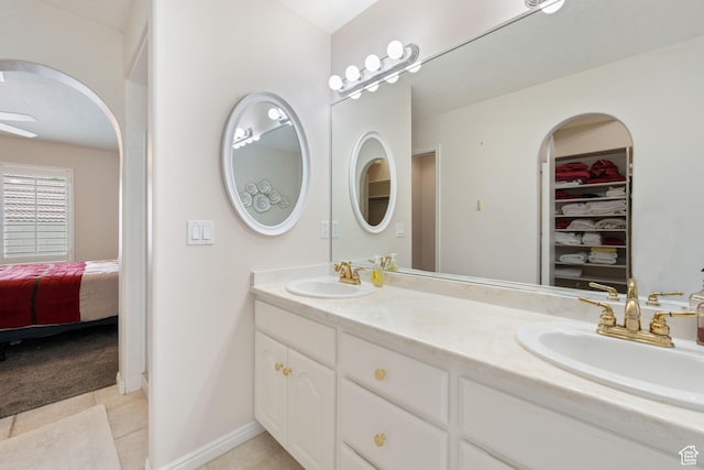 ensuite bathroom featuring tile patterned flooring, double vanity, a walk in closet, and baseboards