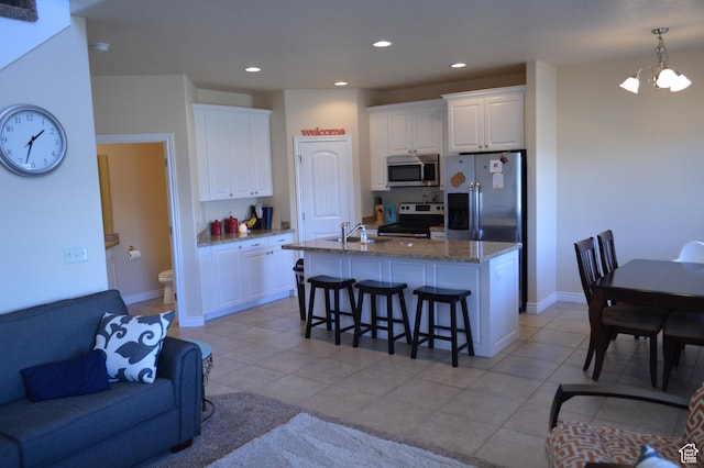 kitchen featuring appliances with stainless steel finishes, a breakfast bar, white cabinetry, stone counters, and recessed lighting
