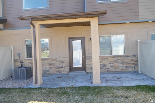 doorway to property with stone siding, cooling unit, fence, and a patio