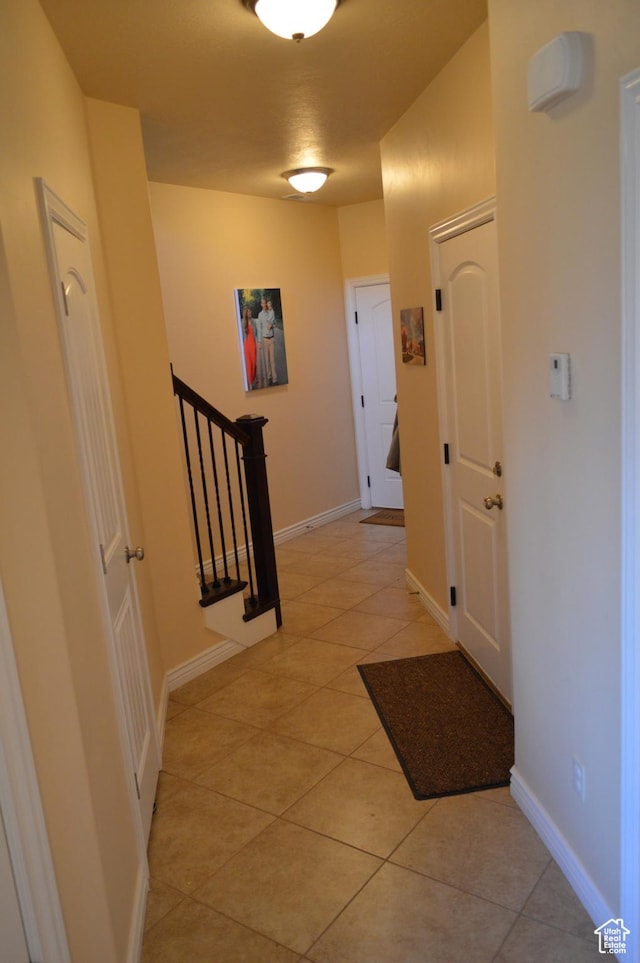 hallway with light tile patterned flooring, baseboards, and stairway