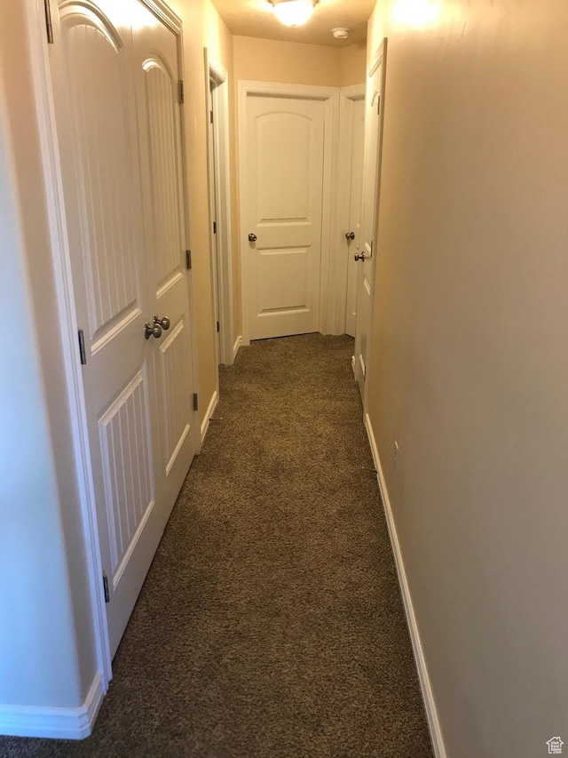 hall featuring baseboards and dark carpet