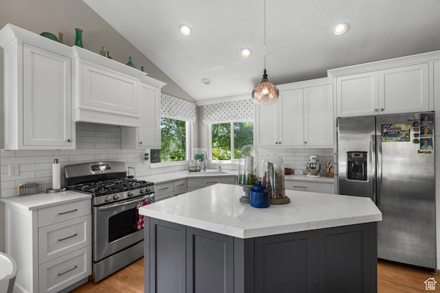 kitchen featuring appliances with stainless steel finishes, vaulted ceiling, backsplash, white cabinetry, and a center island