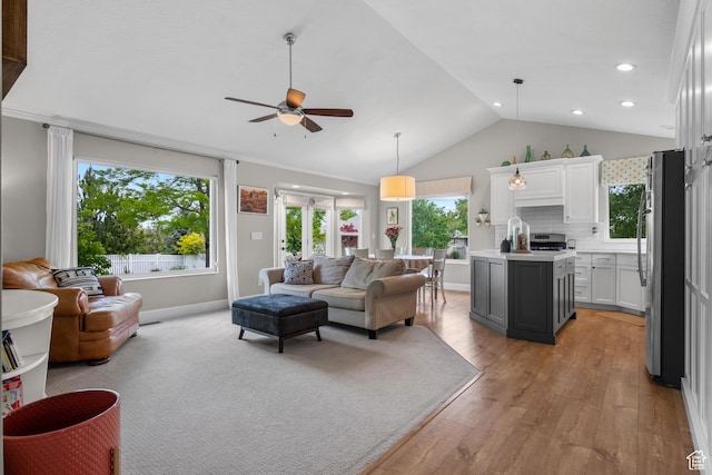 living room featuring vaulted ceiling, ceiling fan, healthy amount of natural light, light wood-style flooring, and baseboards