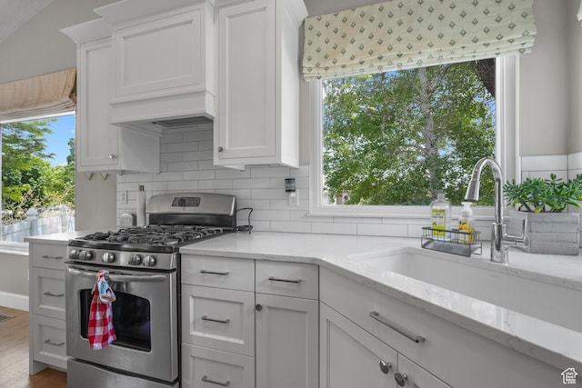 kitchen featuring stainless steel gas range, backsplash, white cabinetry, and a sink