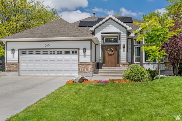 view of front of property featuring a front yard, concrete driveway, a garage, roof with shingles, and solar panels