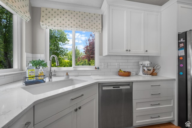 kitchen featuring stainless steel appliances, a sink, tasteful backsplash, white cabinetry, and light stone countertops