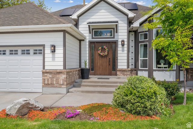 view of exterior entry featuring brick siding, roof mounted solar panels, and a shingled roof