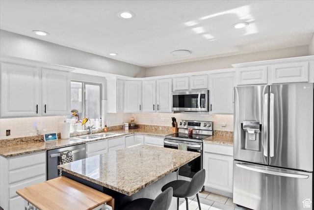 kitchen with stainless steel appliances, a sink, a breakfast bar area, backsplash, and recessed lighting
