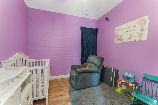bedroom featuring wood finished floors, a nursery area, and brick wall