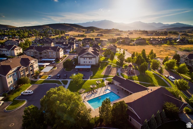 aerial overview of property's location featuring mountains, a pool, and nearby suburban area