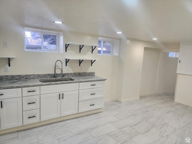kitchen featuring a sink, open shelves, light stone counters, white cabinets, and light marble finish flooring