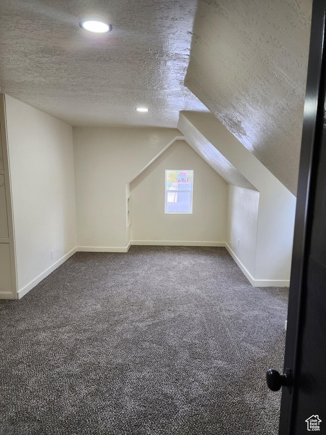 bonus room featuring a textured ceiling, dark carpet, recessed lighting, baseboards, and lofted ceiling