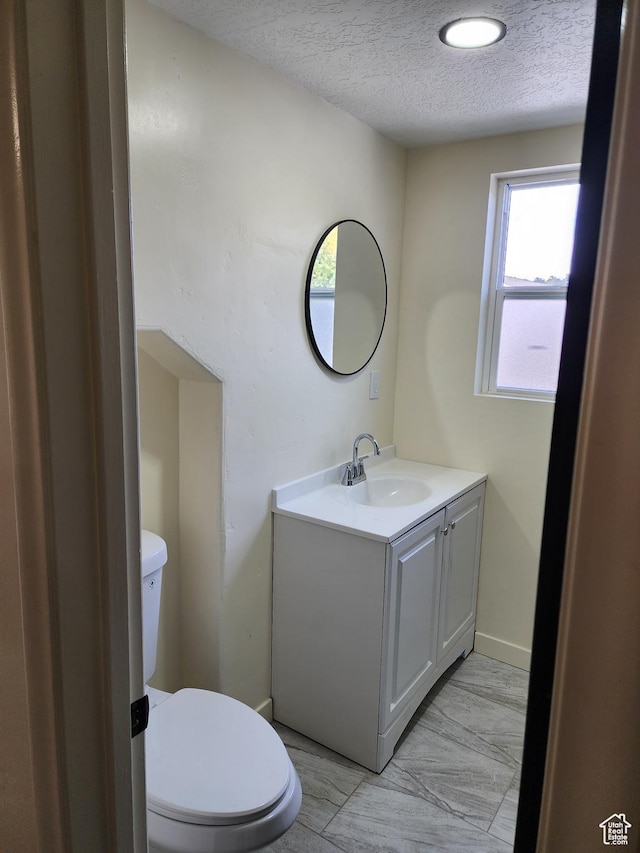 half bathroom featuring a textured ceiling, toilet, vanity, and baseboards