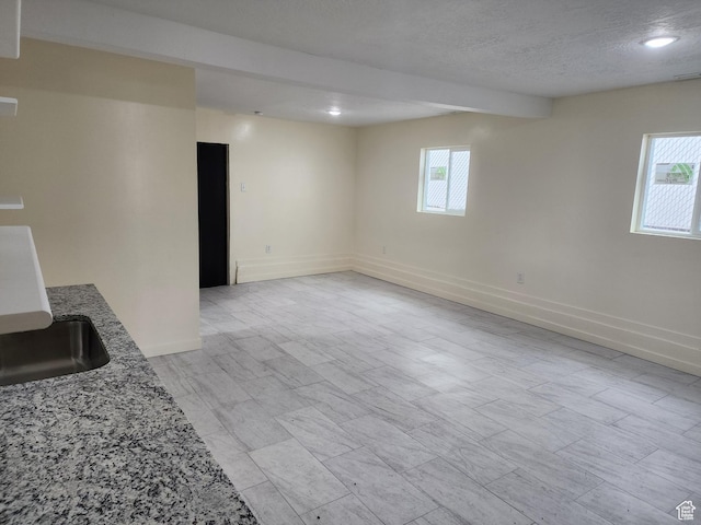 unfurnished living room featuring baseboards, a textured ceiling, recessed lighting, and a sink