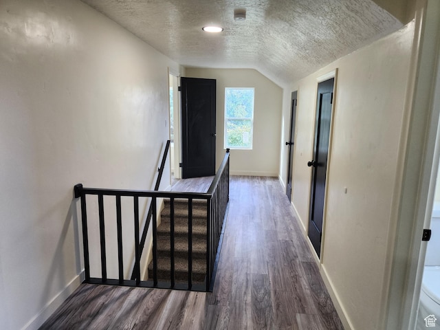 hallway with an upstairs landing, wood finished floors, baseboards, a textured ceiling, and lofted ceiling