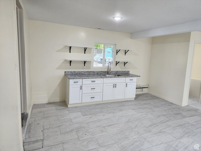 kitchen with open shelves, a sink, light stone counters, white cabinetry, and baseboards