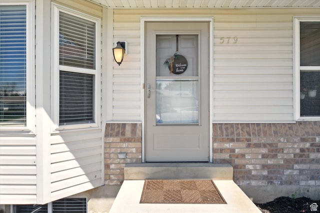 view of exterior entry featuring brick siding and covered porch