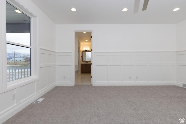 spare room featuring a decorative wall, recessed lighting, light carpet, a ceiling fan, and wainscoting