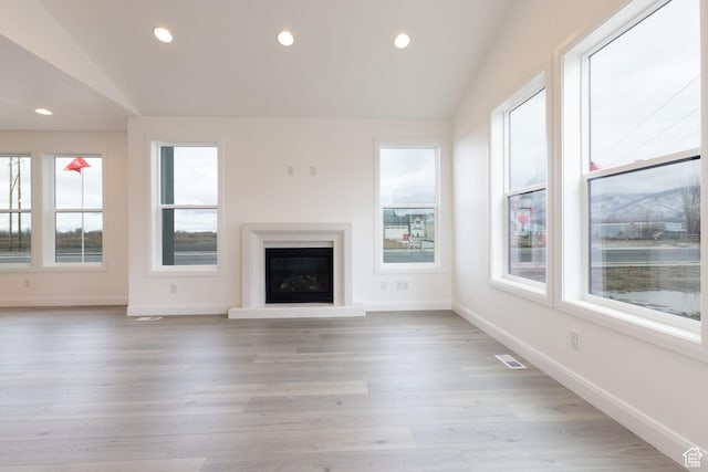 unfurnished living room featuring vaulted ceiling, a glass covered fireplace, baseboards, recessed lighting, and light wood-style floors