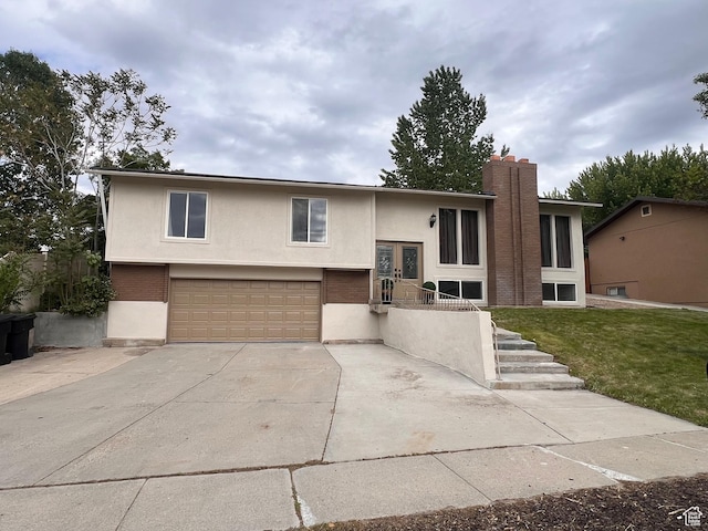 bi-level home with a garage, stucco siding, driveway, a front yard, and a chimney