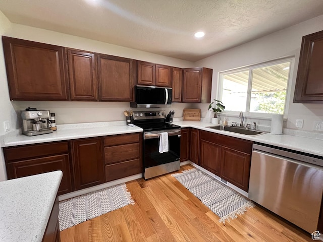 kitchen with stainless steel appliances, a sink, light countertops, light wood-style floors, and recessed lighting