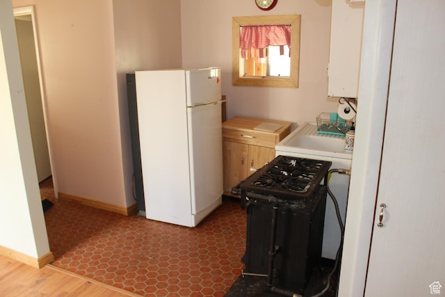 kitchen featuring freestanding refrigerator, light countertops, baseboards, gas range, and water heater