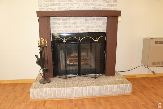 detailed view of a brick fireplace, baseboards, wood finished floors, and heating unit