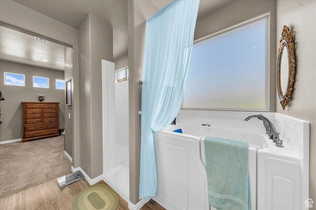bathroom featuring wood finished floors, a garden tub, and baseboards