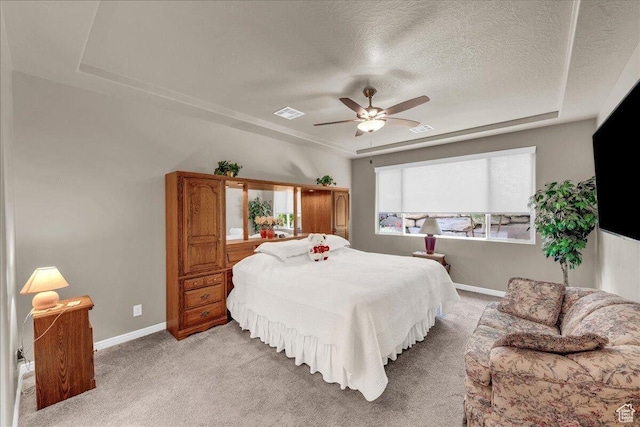 bedroom featuring a tray ceiling, light colored carpet, a textured ceiling, baseboards, and ceiling fan