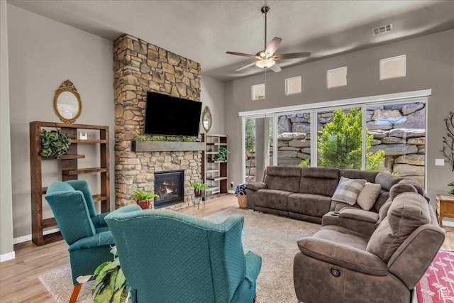 living area with ceiling fan, a fireplace, wood finished floors, a textured ceiling, and baseboards