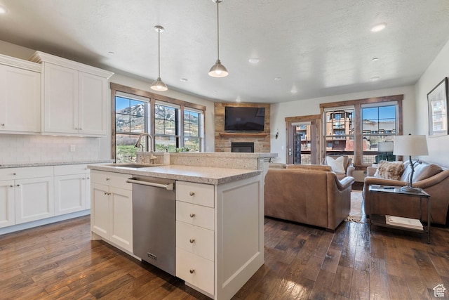 kitchen with a sink, dishwasher, open floor plan, a stone fireplace, and dark wood finished floors