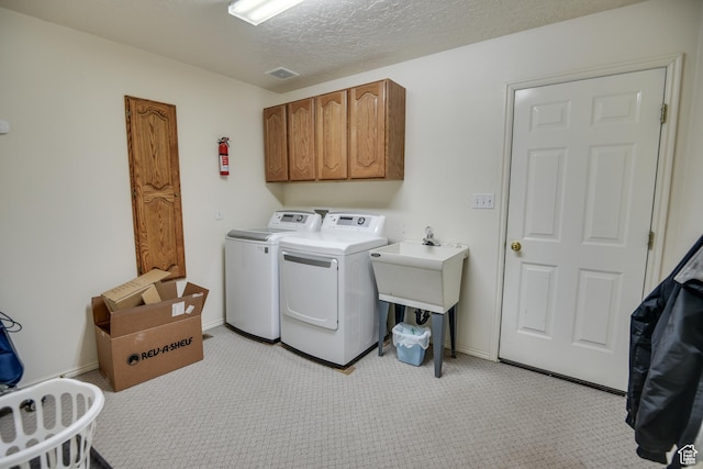 washroom featuring washer and clothes dryer, light carpet, cabinet space, and a textured ceiling