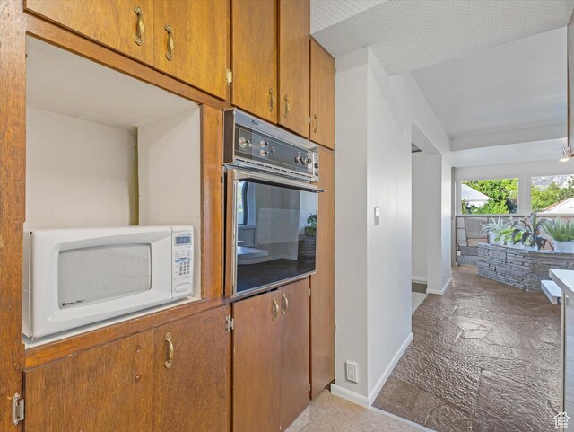 331 N K St, Salt Lake City, UT 84103 - kitchen featuring white microwave, wall oven, baseboards, brown cabinetry, and stone finish floors