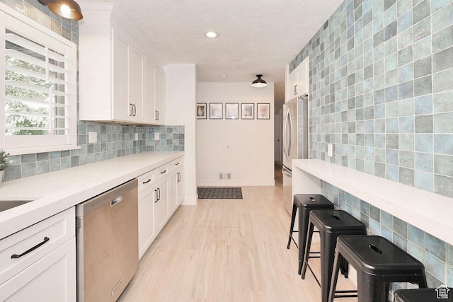 kitchen with stainless steel appliances, white cabinetry, light countertops, tile walls, and light wood-style flooring
