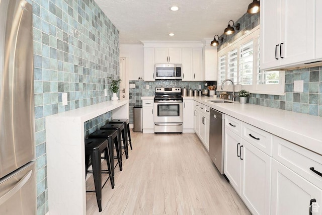 kitchen featuring stainless steel appliances, a sink, decorative backsplash, light wood-type flooring, and white cabinets