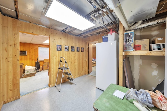 unfinished basement featuring wooden walls, freestanding refrigerator, and tile patterned floors