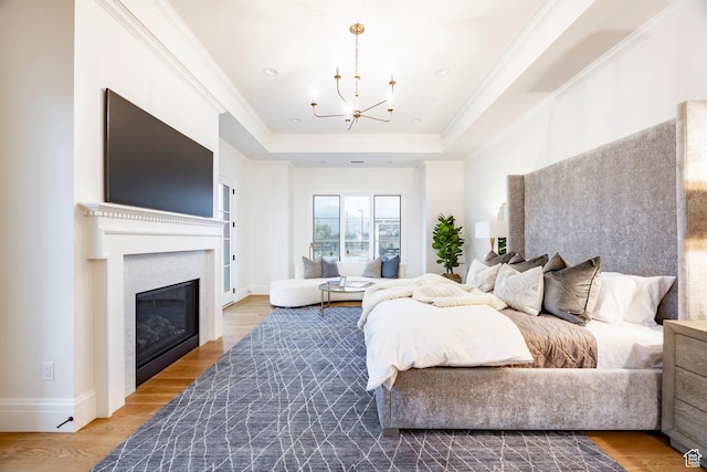 bedroom featuring a chandelier, a raised ceiling, a glass covered fireplace, wood finished floors, and baseboards