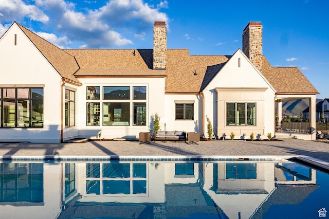back of house featuring a patio area, an outdoor pool, a chimney, roof with shingles, and stucco siding