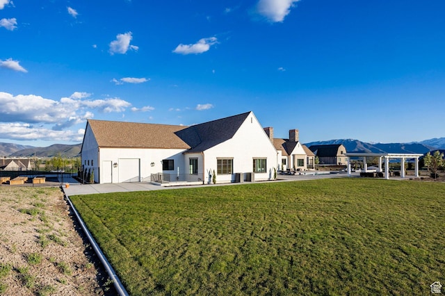 rear view of property featuring a mountain view, stucco siding, an attached garage, a chimney, and driveway