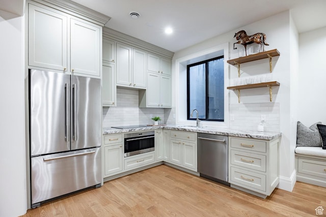 kitchen with stainless steel appliances, a sink, backsplash, light wood-style floors, and light stone countertops