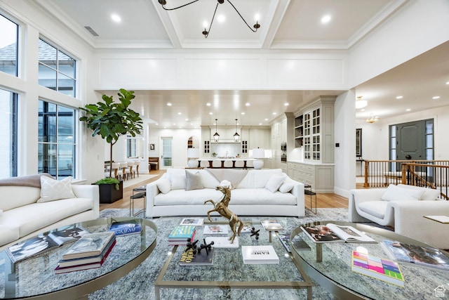 living room featuring a chandelier, a towering ceiling, light wood-type flooring, crown molding, and recessed lighting