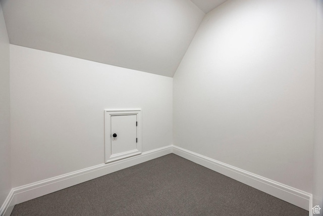 additional living space featuring vaulted ceiling, dark colored carpet, and baseboards