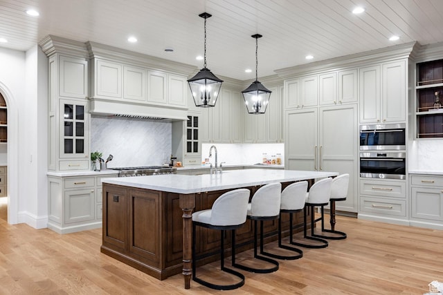 kitchen with a breakfast bar area, light wood finished floors, a center island with sink, recessed lighting, and decorative backsplash