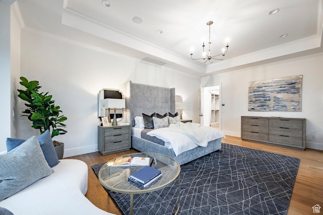 bedroom featuring a tray ceiling, a chandelier, ornamental molding, wood finished floors, and baseboards
