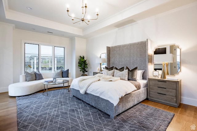 bedroom with a chandelier, a raised ceiling, wood finished floors, ornamental molding, and baseboards