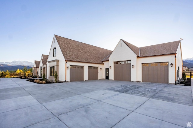 view of property exterior with an attached garage, concrete driveway, roof with shingles, a mountain view, and stucco siding