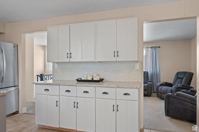 kitchen with freestanding refrigerator, decorative backsplash, white cabinets, open floor plan, and light stone countertops