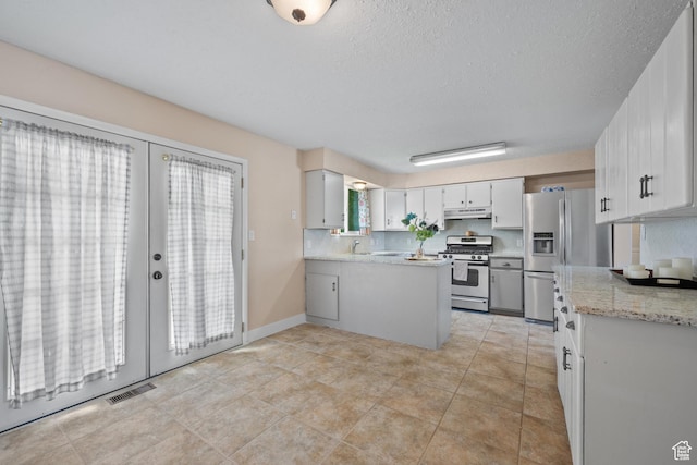 kitchen with appliances with stainless steel finishes, under cabinet range hood, french doors, a peninsula, and white cabinetry